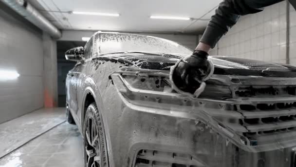 Detallado del coche - el hombre lava los faros de un coche con una mano cubierta con un guante de lavado especial, primer plano. - Metraje, vídeo