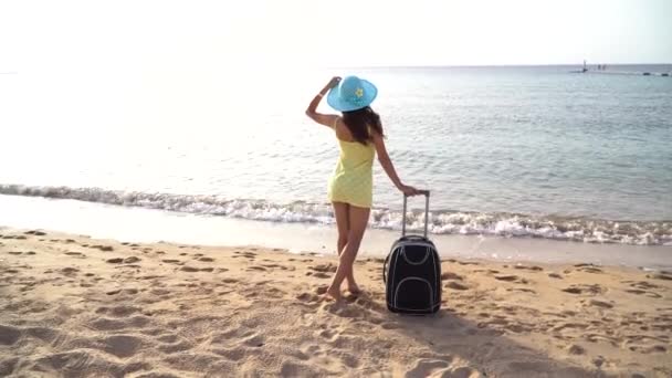 Hermosa mujer en un sombrero con maleta contra el mar durante las vacaciones de verano. mujer feliz mirando al mar. Vídeo Full HD de imágenes de movimiento - Imágenes, Vídeo