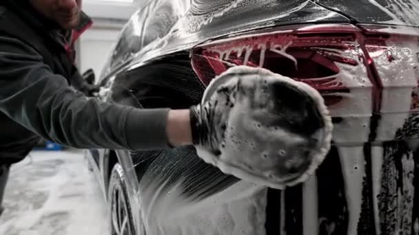 Car detailing - the man washes backlights of a car with a hand covered with a special wash glove, close-up. - Footage, Video