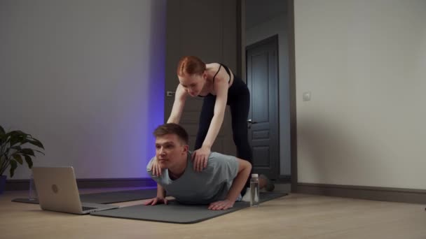 Une fille en vêtements de sport aide un gars dans un cours de yoga, au ralenti - Séquence, vidéo