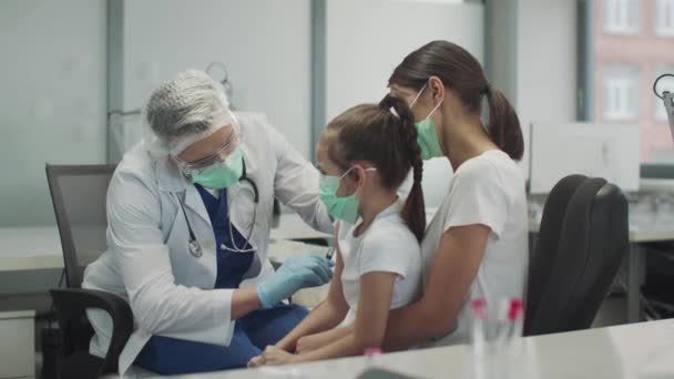Un médico amable en gafas protectoras y una máscara le ha dado al niño una inyección en el brazo y asiente aprobadamente a ella, en cámara lenta. - Imágenes, Vídeo