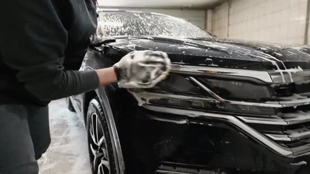 Auto detaillering - de man wast koplampen van een auto met een hand bedekt met een speciale washandschoen, close-up. - Video