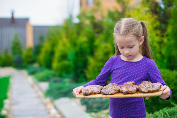 Menina adorável com bifes grelhados nas mãos ao ar livre
 - Foto, Imagem