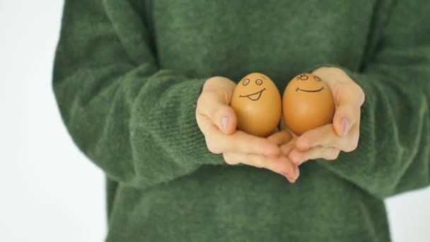 Jeune femme en pull vert montre des œufs avec le visage dessiné à la main avec un sourire du panier de paille, préparation de Pâques, concepts d'humeur de vacances - Séquence, vidéo