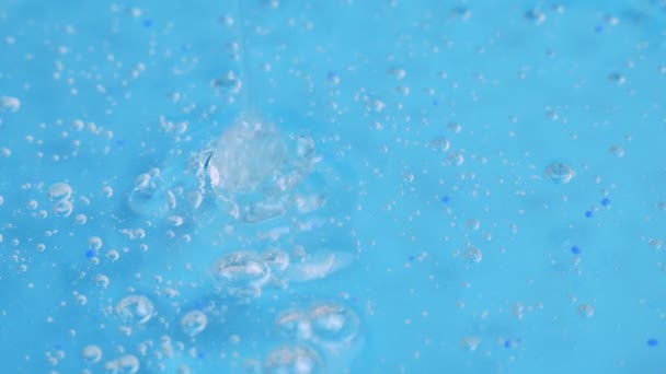 Um toque de gel cosmético transparente com pequenas bolhas goteja na superfície azul. soro facial, creme anti-envelhecimento, shampoo capilar, gel antibacteriano, ácido hialurônico - Filmagem, Vídeo