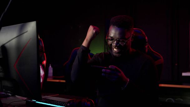 En el club de juego, un negro juega un juego en línea en un teléfono inteligente, gana y es feliz - Foto, imagen