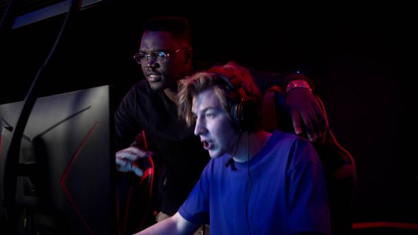 Um jogador experiente de esports mostra a seu amigo de pele escura como jogar um jogo de vídeo online em um clube de computador - Foto, Imagem