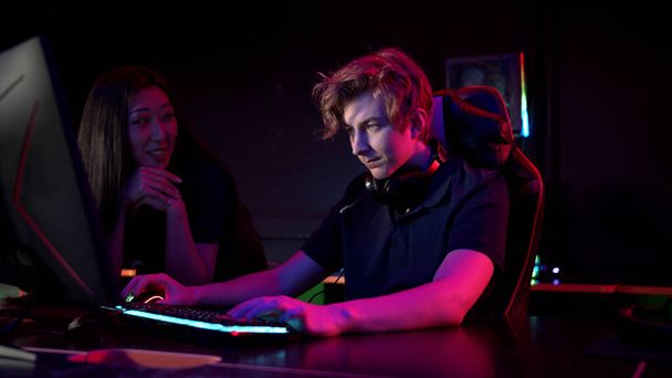 Um jovem asiático menina flerta com um cara em um computador clube, ela sorri e oferece ajuda no jogo - Foto, Imagem