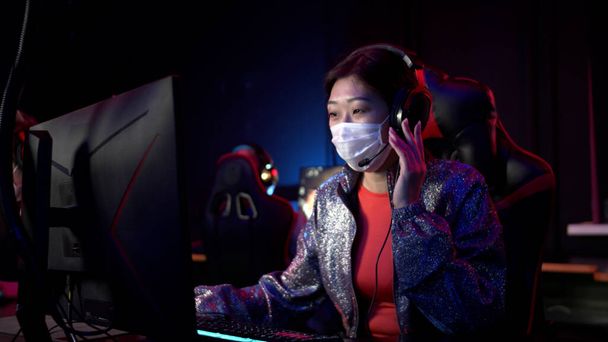 オンラインの最初の顔のシューティングゲームでゲームの初めに、医療マスクのアジアの女の子は、選択する英雄チームと相談します。 - 写真・画像