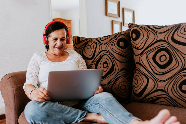 латинская зрелая женщина носить беспроводные наушники, держа смартфон и слушать онлайн музыку дома в Мехико - Фото, изображение