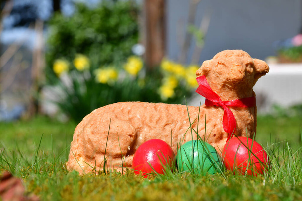 Huevos de Pascua y un cordero de Pascua al horno en un prado con flores en el fondo - Foto, Imagen