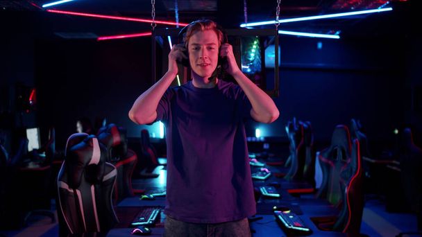 Um jovem está se preparando para um torneio de jogos online, ele coloca fones de ouvido e ajusta o microfone - Foto, Imagem