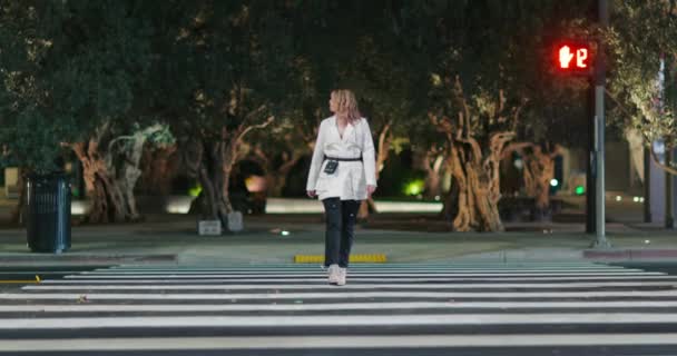 Nezávislá žena ve stylové značkové bundě přecházející silnici v noci města záběry - Záběry, video