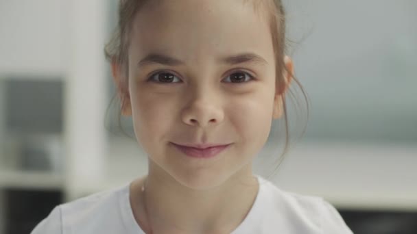 Grande retrato de uma pequena menina sorridente de olhos castanhos em uma camiseta branca - Filmagem, Vídeo