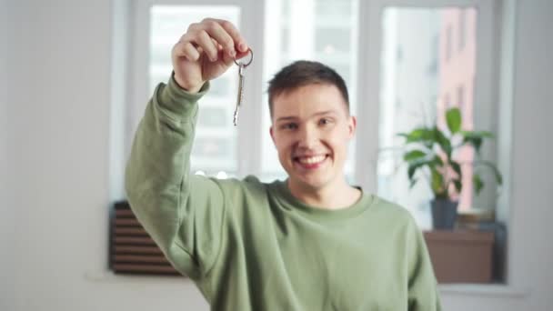 Un jeune homme se tient dans une pièce blanche vide et secoue les clés avec un sourire - Séquence, vidéo
