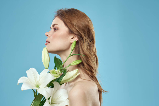 Woman with a bouquet of white flowers on a blue background naked shoulders beautiful face - Photo, Image