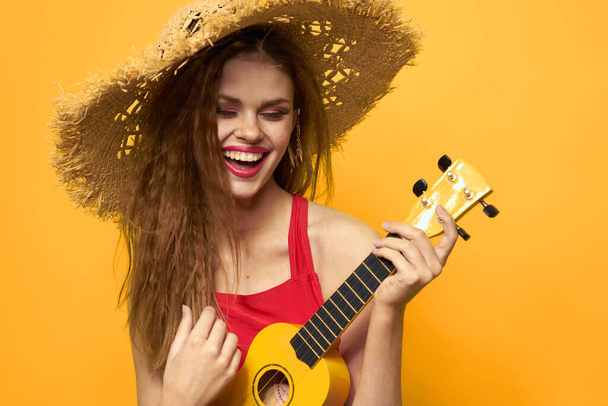 woman in red hat ukulele in hands lifestyle summer red t shirt yellow background - Zdjęcie, obraz