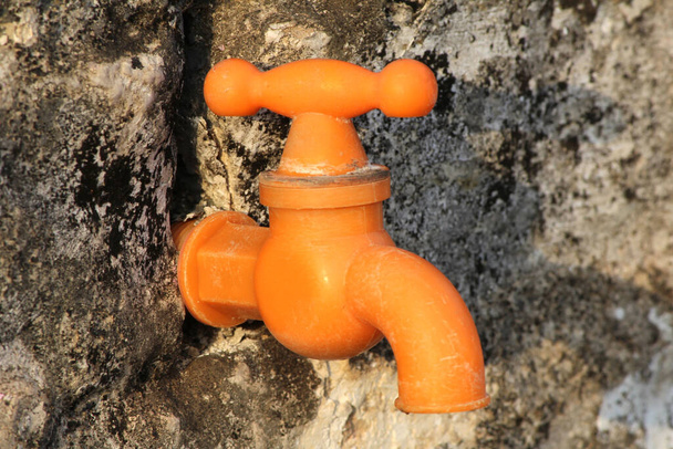 ein orangefarbener Wasserhahn isoliert auf Steinhintergrund - Foto, Bild