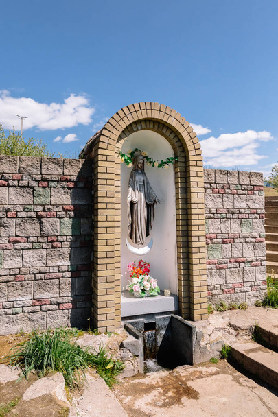 Wall with Niche in which there is a sculpture of the Holy Virgin Mary made of bronze in crown and on the moon. Nearby there is a source of holy water - spring. The main person in the Christian faith. - Photo, Image