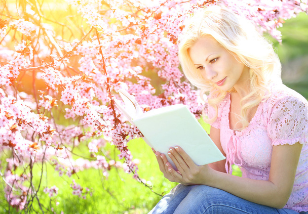 Girl with Book. Blonde Young Woman and Cherry Blossom. Outdoor.  - Foto, afbeelding