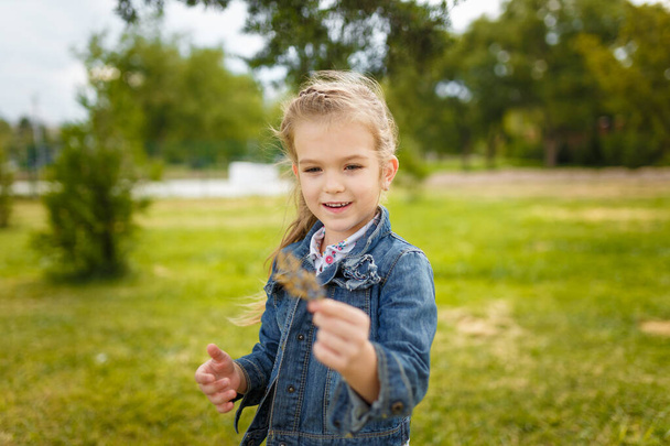 Holčička drží list, jemně zaostřený záběr zblízka. Portrét šťastně se usmívajícího dítěte - Fotografie, Obrázek