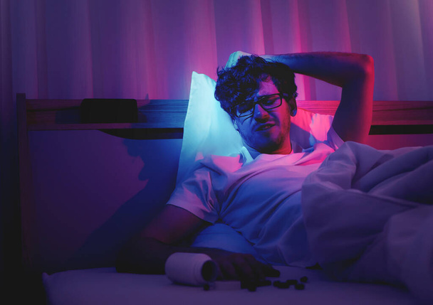 Depressziós álmatlanság fehér férfi tartja a fejét az ágyon késő este Fekete orvosi tabletták stressz és öngyilkosság koncepció. - Fotó, kép