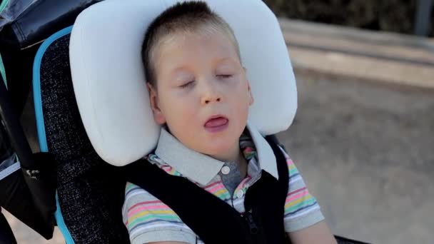 Acercamiento niño pequeño sentado en silla de ruedas especial al aire libre. Niño con discapacidad física - Imágenes, Vídeo