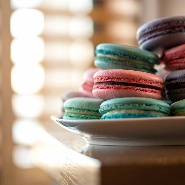 Macaroons French dessert. Colored pastries or cookies at table against of sunny morning window on background. Female fancy. Blank or template for banner or greeting card. Copy space - Photo, Image