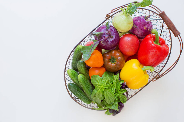 Металлическая корзина со свежими овощами на белом фоне. Свежий перец, помидоры, огурцы, листья базилика и кольраби в металлической корзине - Фото, изображение