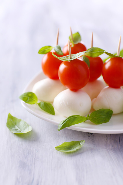 Tasty mozzarella cheese with basil and tomatoes on plate, on wooden table - Photo, Image