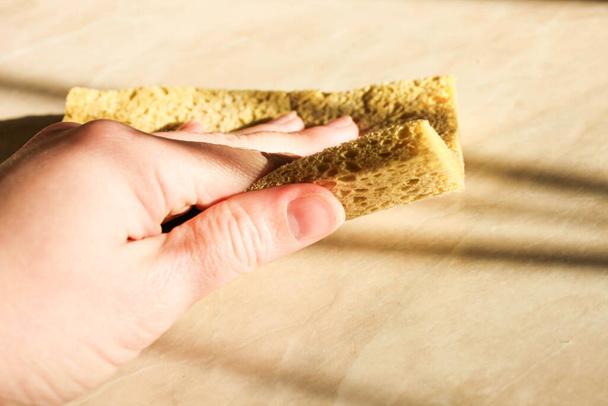 Woman's hand wipes the tabletop with a yellow sponge close-up. - Photo, Image