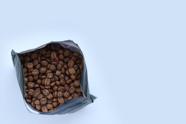 Verpackt frisch geröstete Kaffeebohnen. Kaffee in einem Beutel. Ein Bündel Kaffeebohnen auf weißem Hintergrund, Copywriting Space. Das Aroma von Kaffee.Körner.Schwarze Packung auf weißem Hintergrund mit Kaffeekörnern - Foto, Bild
