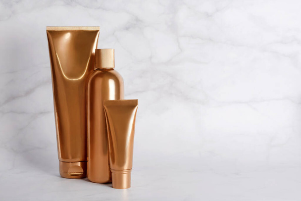 Golden bottles, cosmetic products on marble background. Luxury beauty style. Gold cosmetic containers. Mockup bottles, cosmetics branding, hair or body care concept. Copy space, empty place for text - Photo, Image