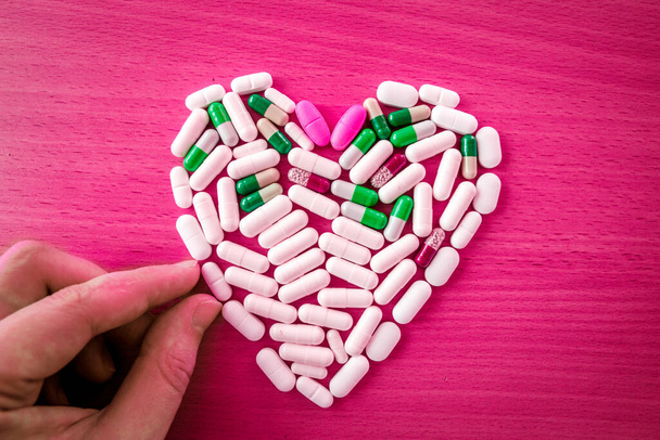 Concepto de cuidado del corazón. Un montón de pastillas en forma de corazón sobre fondo rosa brillante - Foto, imagen