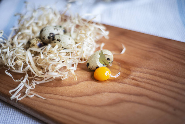 fresh quail eggs on a wooden board, quail eggs for a delicious easter holiday, raw homemade quail egg smashed on a kitchen board, raw yolk and egg white - Photo, Image