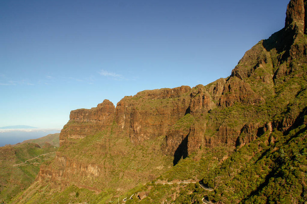 La strada sinuosa che scende al burrone Masca (canyon) ai piedi delle cime rocciose, Tenerife, Isole Canarie, Spagna. Isola di La Palma all'orizzonte circondata da nuvole sullo sfondo. - Foto, immagini