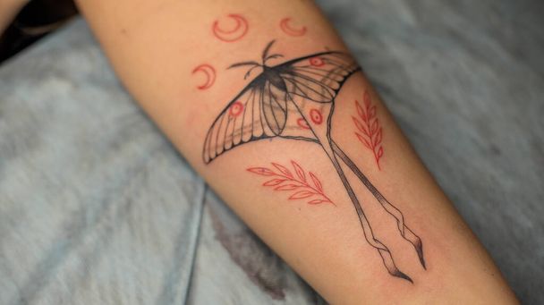 Il tatuaggio principale disegna la vernice rossa sul tatuaggio dei clienti. Tatuaggio artista in possesso di una macchina tatuaggio rosa in guanti sterili neri e lavorando sul tappeto blu professionale. - Foto, immagini