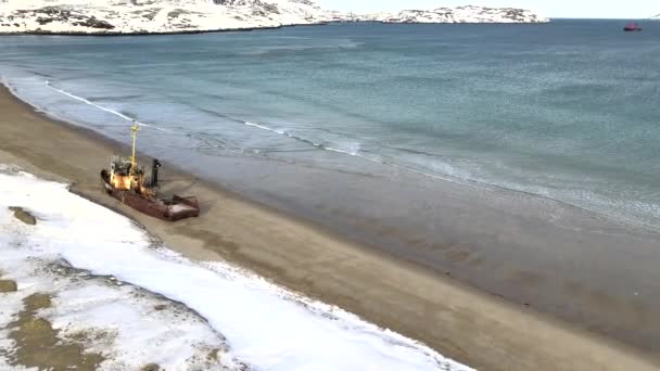 冬の雪の季節に海岸で溺死した古い難破船の空中トップビュー。映像だ。ロシアのTererberkaの雪の砂の海岸近くの冷たい水の中の荒廃したボートの空中ビュー - 映像、動画