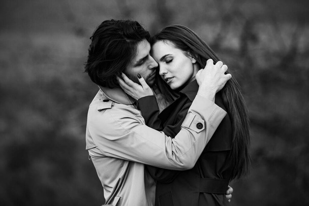 Beautiful sensual portrait of young stylish couple in love. Image of adorable brunette couple in rain trench coat in park. Happy family - Photo, Image