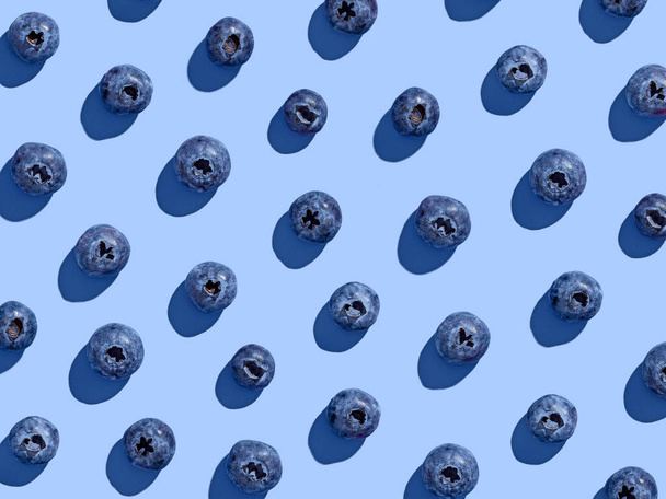 Colorful blueberry pattern on blue background, from above, hard shadow - Photo, Image