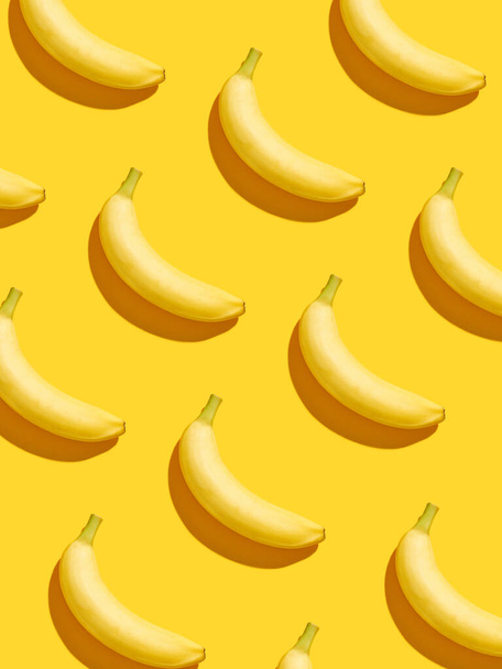 黄色の背景に垂直カラフルなバナナのパターンは、上から、ハードシャドウ - 写真・画像