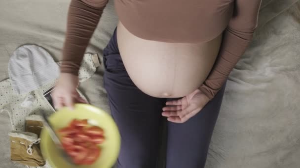 Top vew odottaa raskaana oleva nainen, jolla on suuri vatsa syö tomaatteja kotona - Materiaali, video