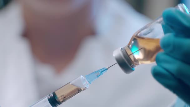 Неузнаваемый врач в защитных синих перчатках, наполняющий стерильный шприц желтым раствором из ампула, эксперименты в лаборатории с потенциальной вакциной. Концепция иммунизации - Кадры, видео