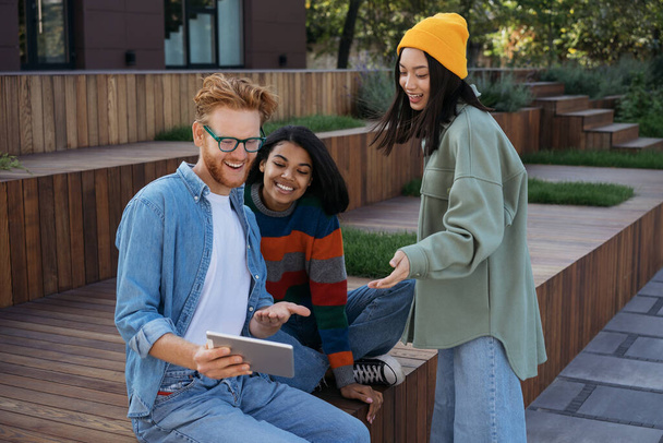 Uśmiechnięci studenci korzystający z tabletu cyfrowego studiujący razem w kampusie uniwersyteckim, koncepcja edukacji. Różnorodne spotkania biznesowe, rozmowy, komunikacja na świeżym powietrzu  - Zdjęcie, obraz