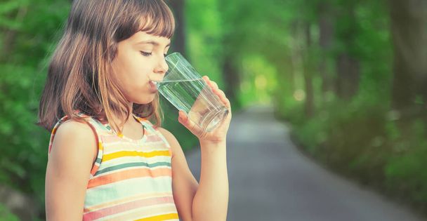 Un bambino beve acqua da un bicchiere sulla natura. Concentrazione selettiva. Bevi.. - Foto, immagini