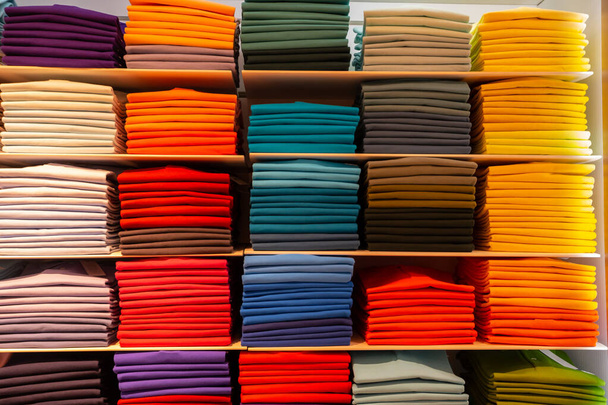 Різнокольоровий одяг складений у стелажі та організований кольоровими діапазонами. Місце ринку - Фото, зображення
