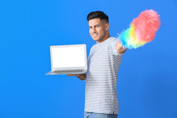 Young man with laptop and dust brush on color background - Photo, Image