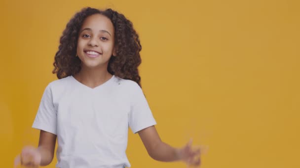 Linda menina adolescente afro-americana apontando para o lado e sorrindo, fundo de estúdio laranja com espaço vazio para maquete - Filmagem, Vídeo