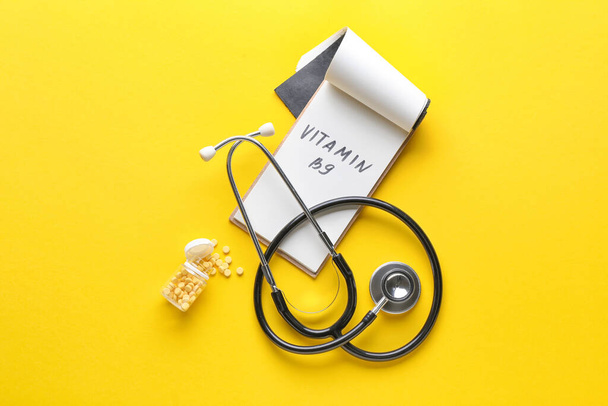 Stetoskop, láhev s pilulky kyseliny listové a text VITAMIN B9 na barevném pozadí - Fotografie, Obrázek