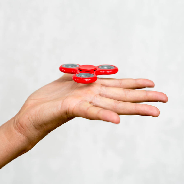 Rode hand spinner. Jongen speelt een populaire speelgoed fidget spinner in zijn hand. Stressverlichting. Anti stress en ontspanning adhd aandacht rage jongen concept - Foto, afbeelding